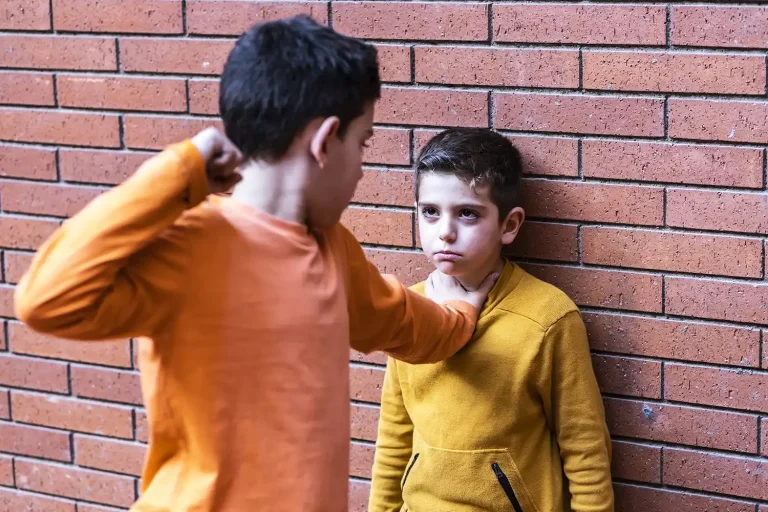 Jongen wordt tegen een muur geduwd door een klasgenoot – voorbeeld van fysiek geweld dat vaak ontstaat na online pesterijen via social media.